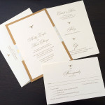 A modern, traditional gold and ivory custom wedding invitation set with insert and reply postcard.