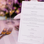 A minimalist, purple and silver custom wedding menu displayed at dinner table for each guest.